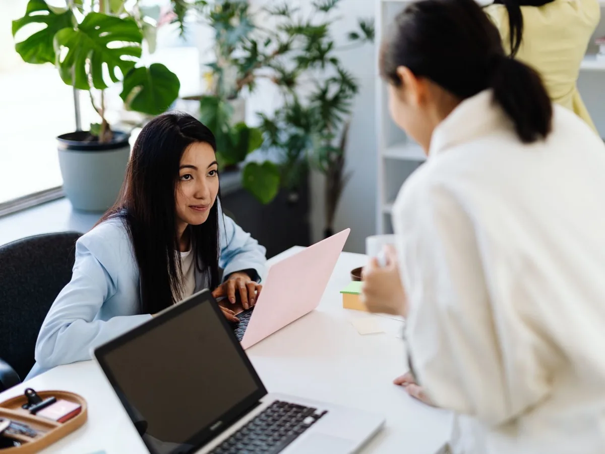 Twee collega's kijken samen naar een laptop aan een bureau bij het raam.