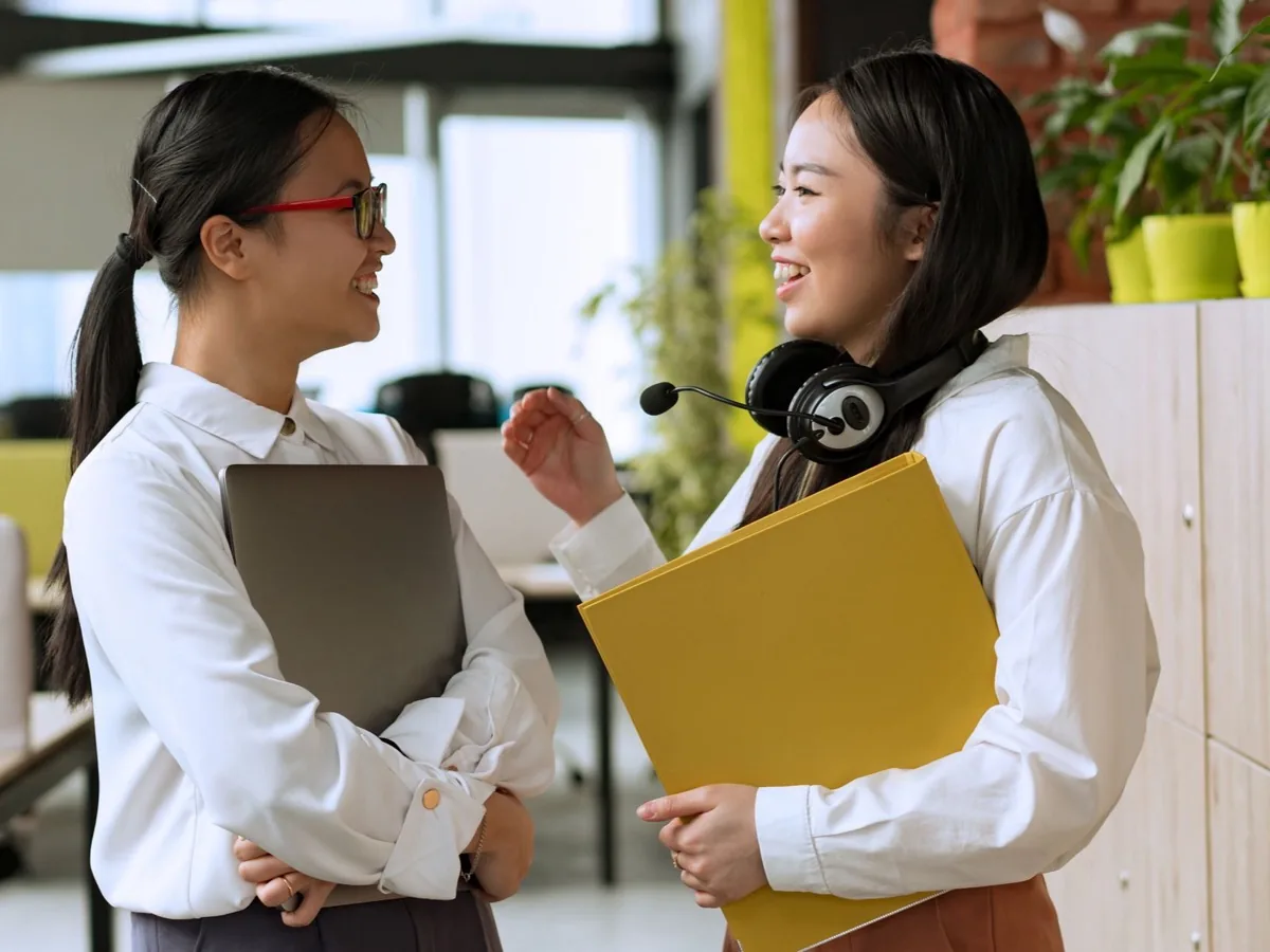 Twee collega's staan met mappen in hun handen te overleggen in een kantoor.