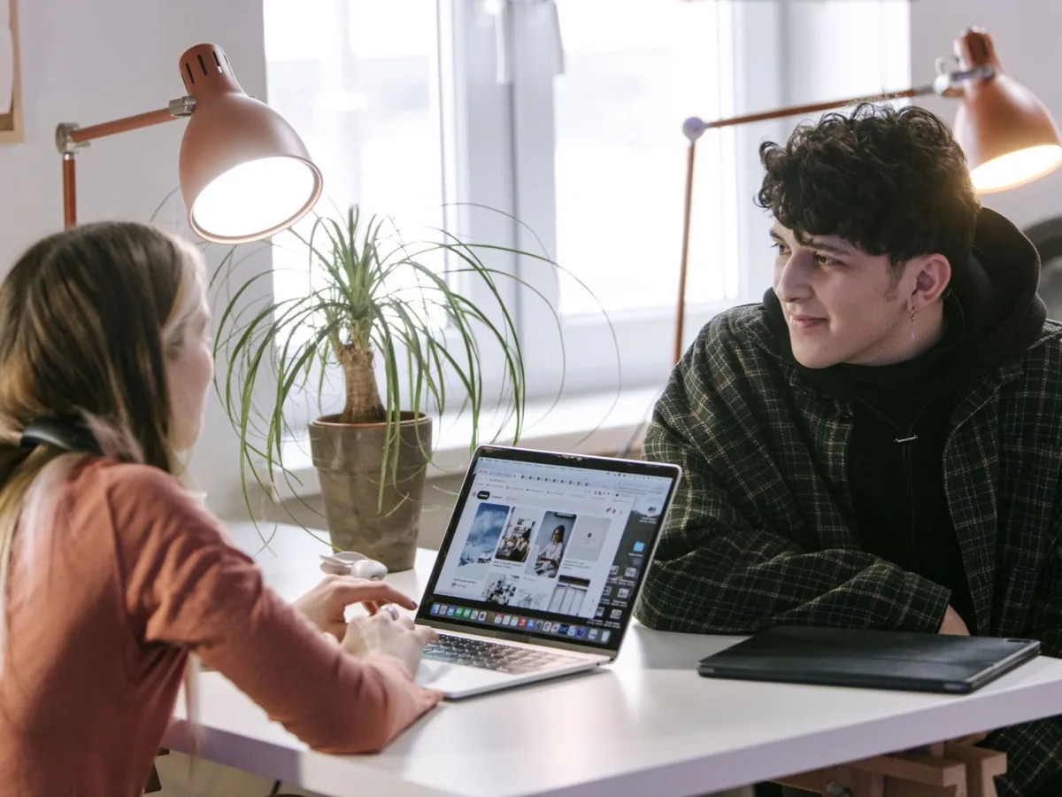 Twee collega's kijken samen naar een laptopscherm onder een bureaulamp.