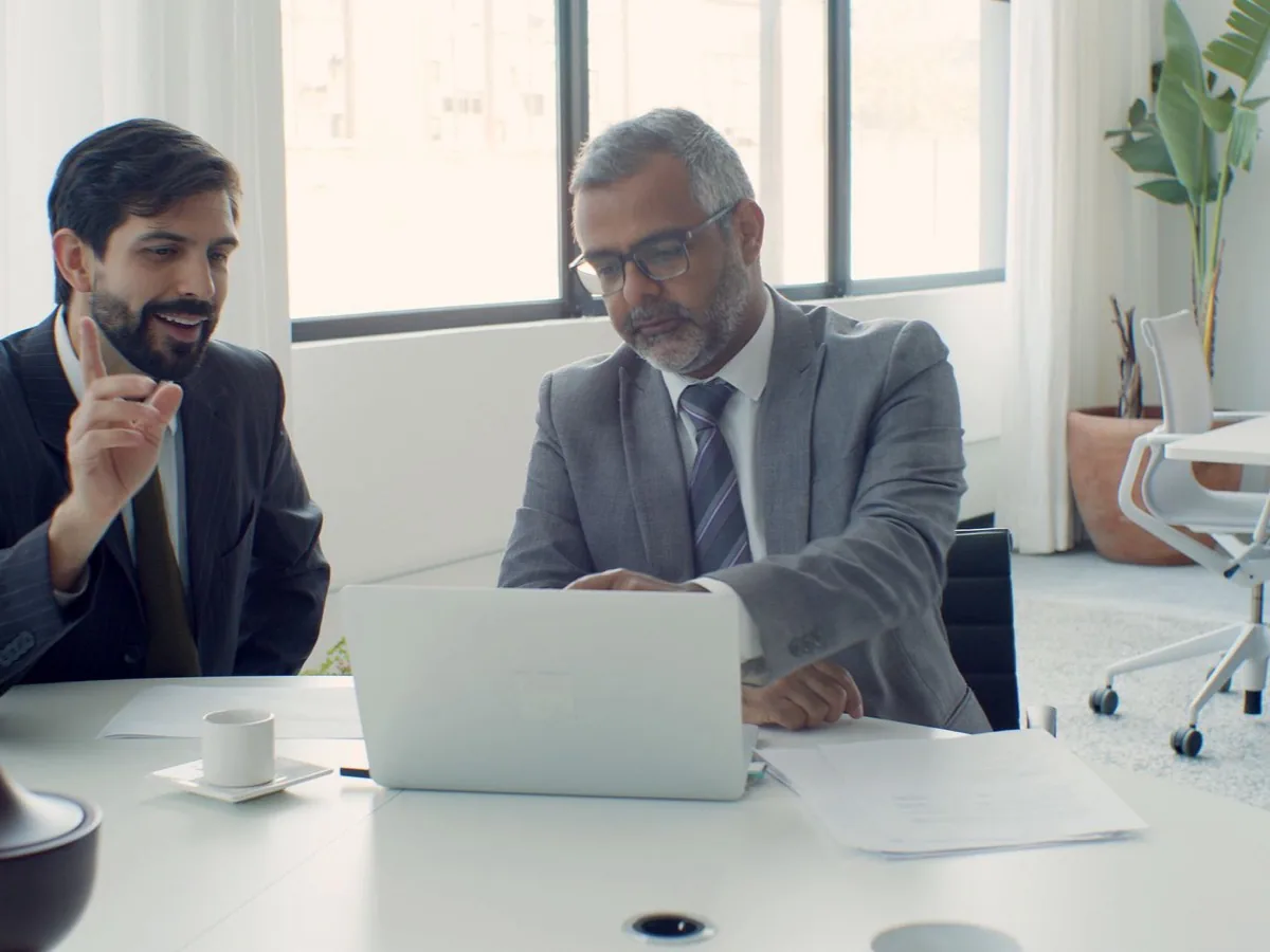 Twee mannen kijken samen naar een laptop aan een tafel.